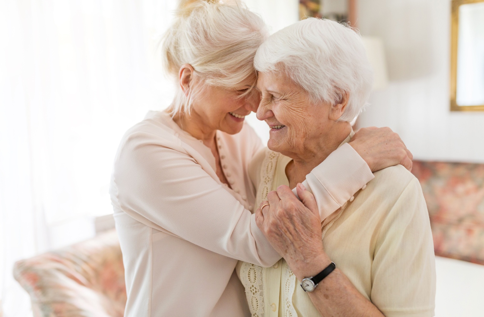 A happy and smiling adult daughter and elderly mother in a warm embrace.