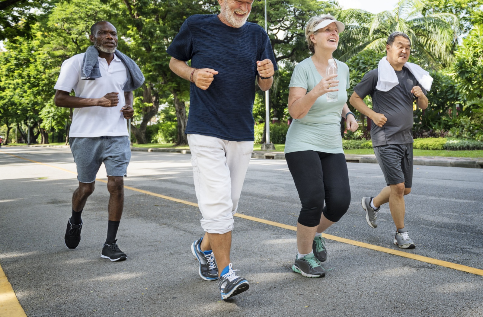 4 older adults smiling while jogging in a park.