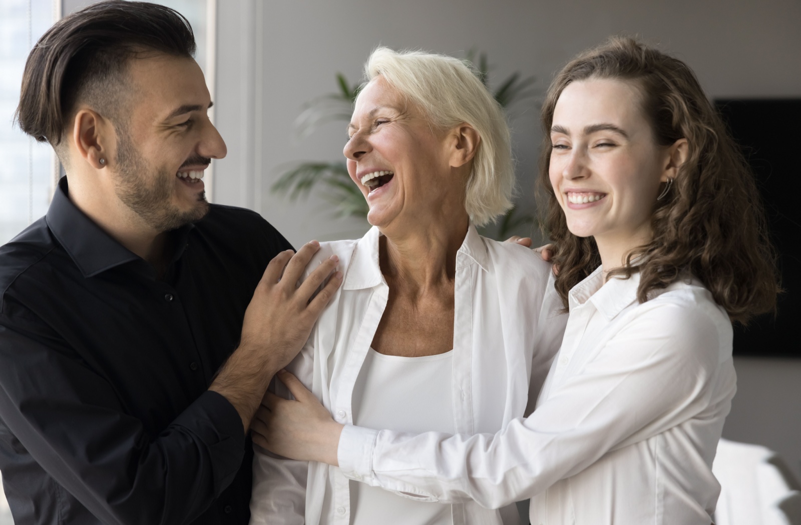 An older adult smiling with their arms around their two laughing adult children.