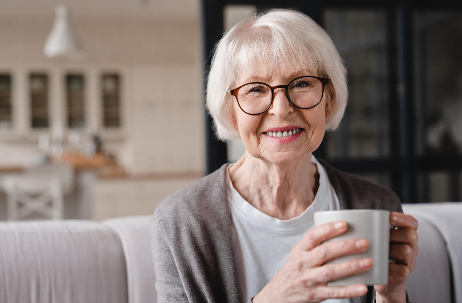 An older adult smiling while drinking coffee in their home in independent living.