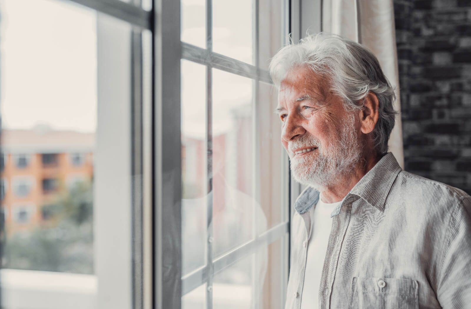 An older adult smiles while looking out the window of their new independent living community