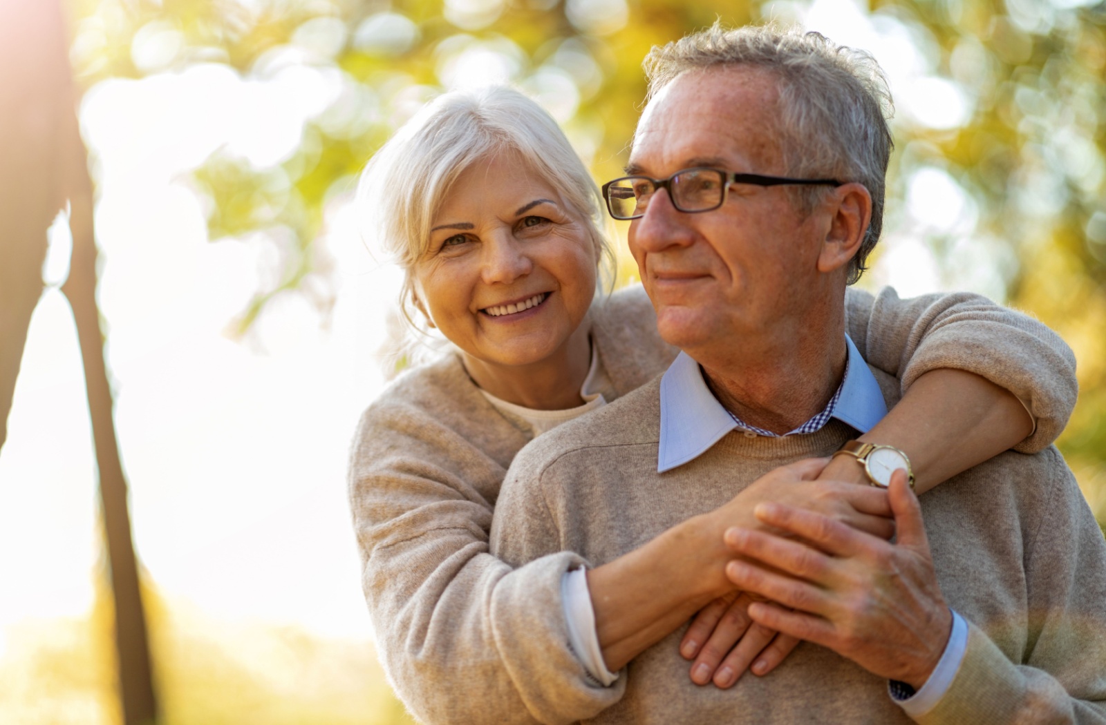 An older adult hugs their spouse and smiles while walking together during an autumn sunset