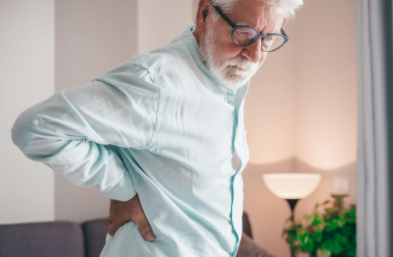 An older adult rubs their lower back while grimacing due to age-related back discomfort
