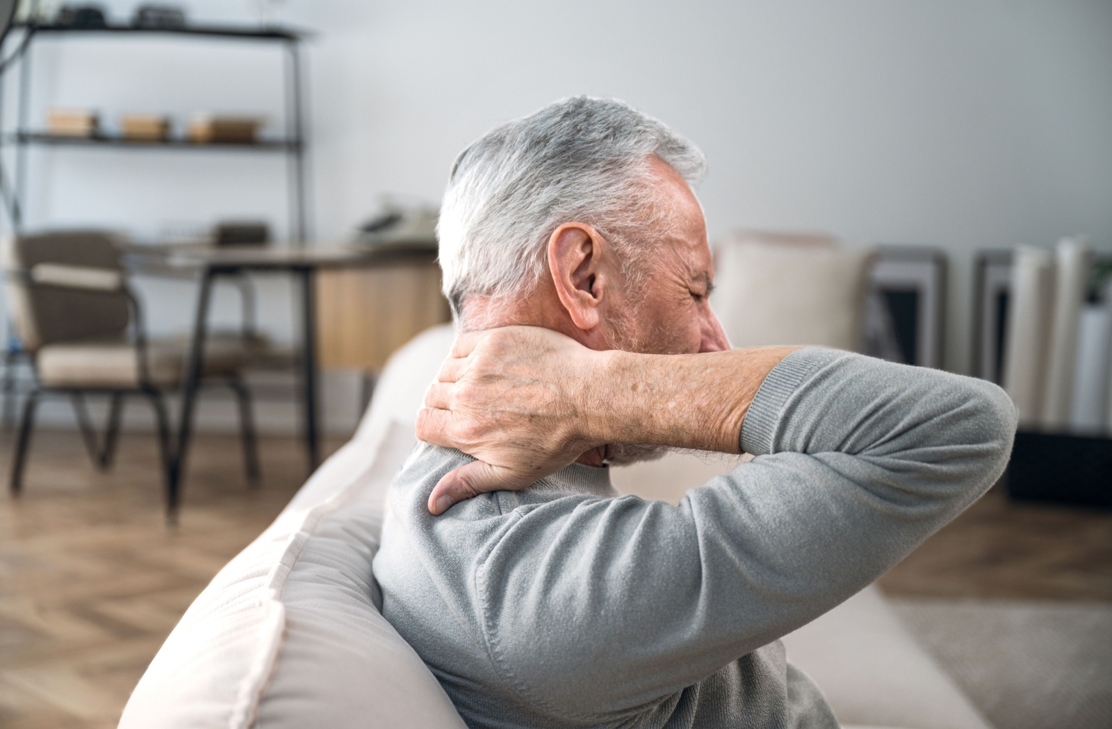 Sitting on the couch, an older adult rubs their neck in discomfort to try and reduce their joint pain