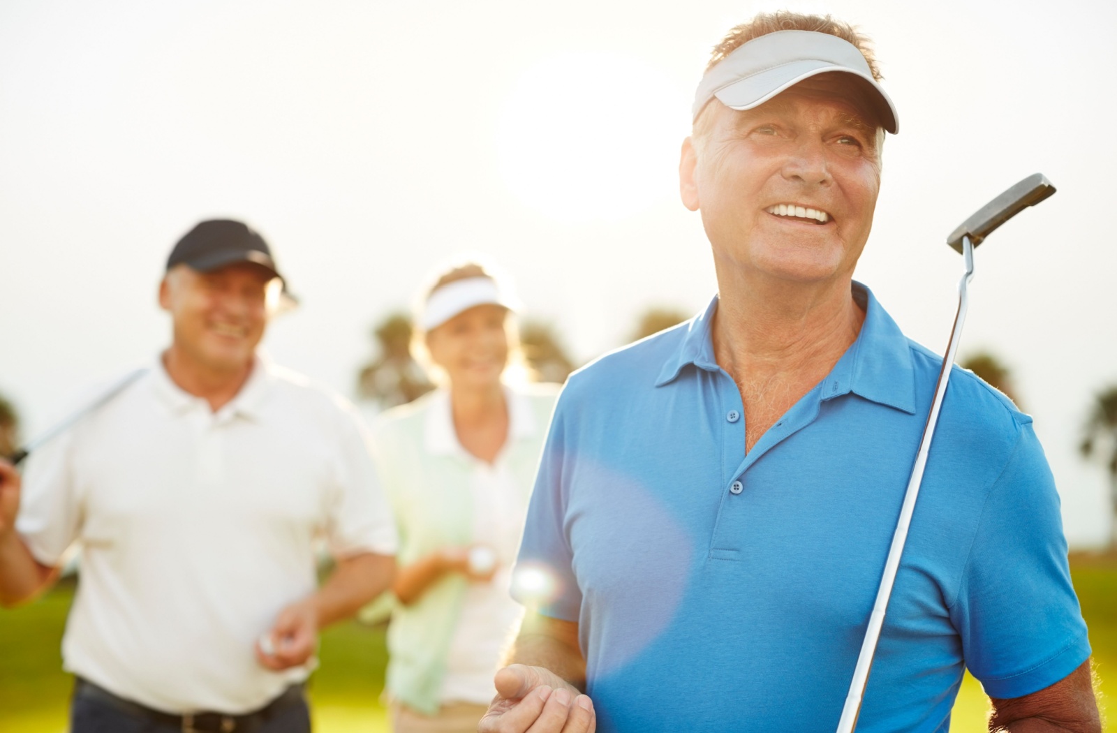 A group of senior adults on a golf course, with a close-up of the one senior in a blue polo, holding a putter.