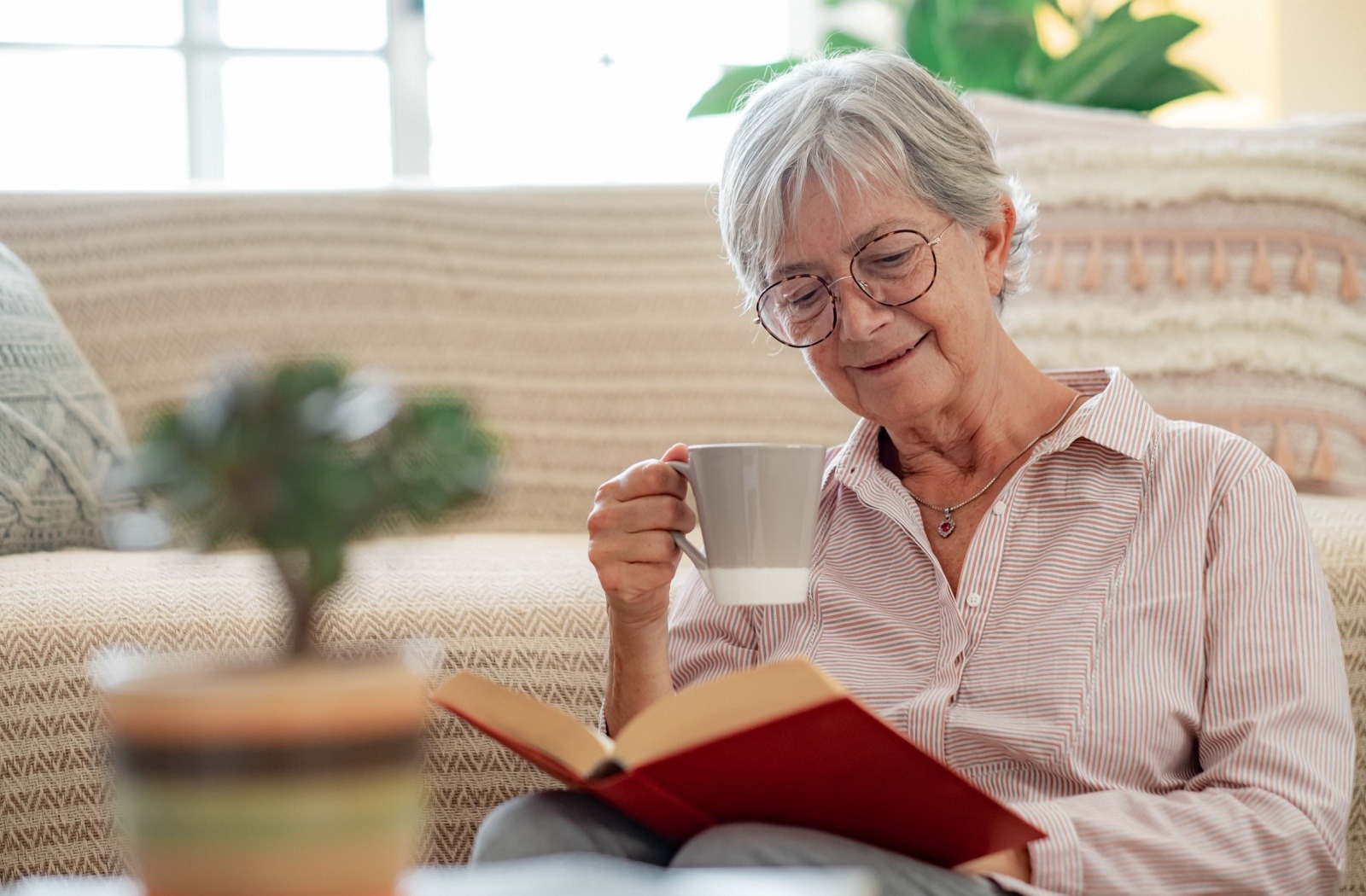 A senior enjoys reading a book while drinking a cup of coffee.