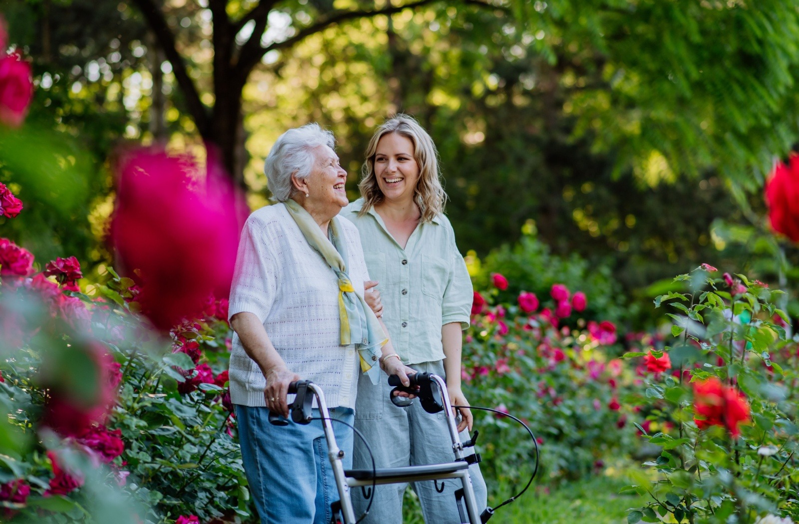 An older adult and their adult child walk together through beautiful community gardens