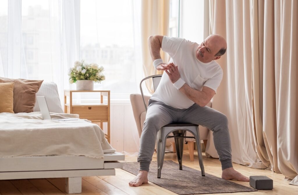 An older adult sits in front of a sunlit window and twists to one side during a chair exercise routine in senior living